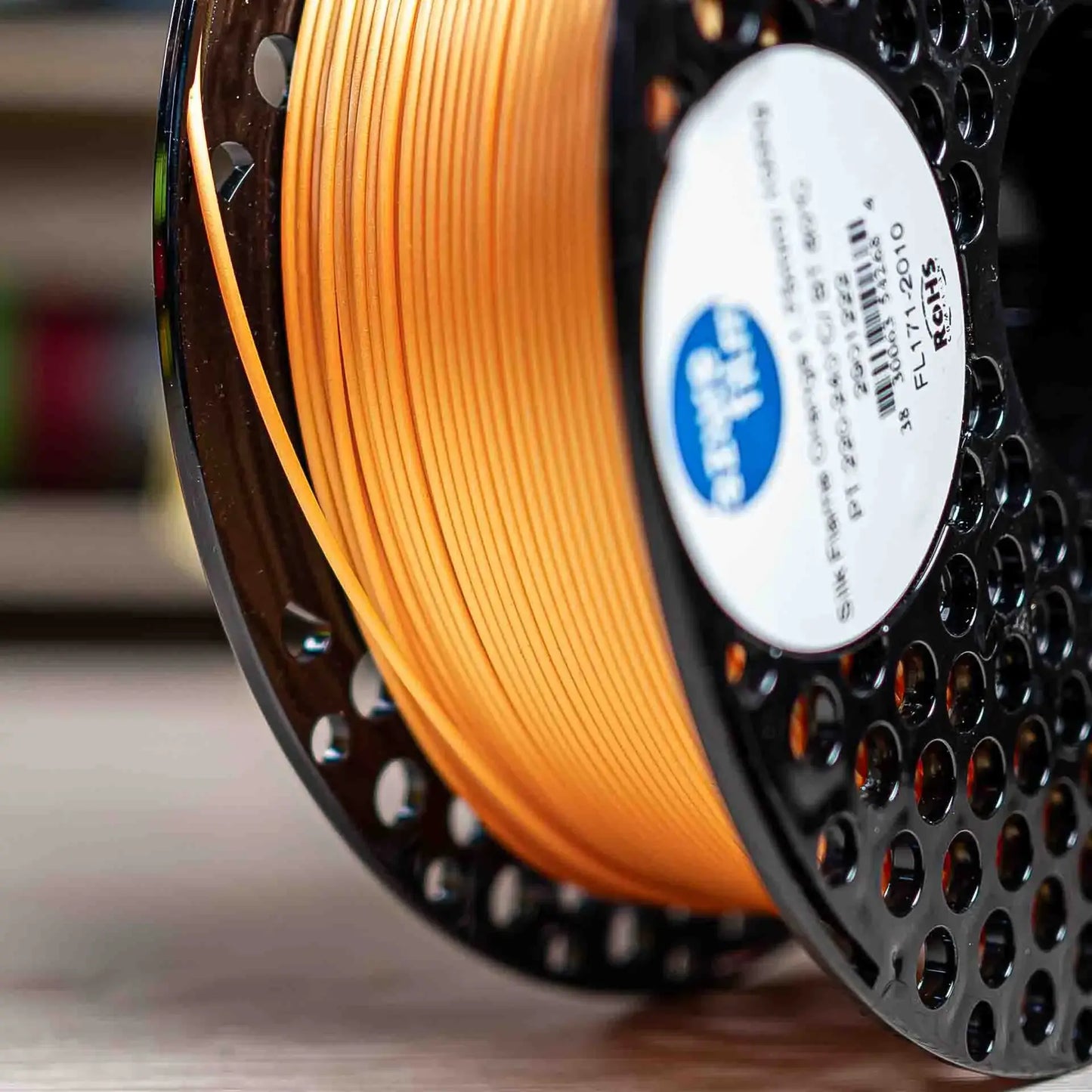 AzureFilm PLA Silk Filament mit seidigem Glanz auf einer Spule, leuchtender oranger Farbton.